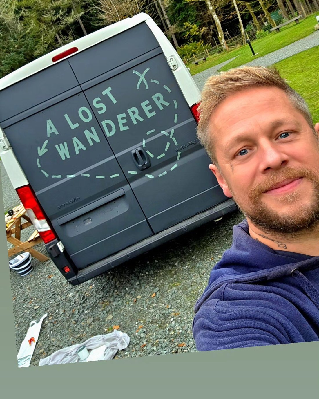 The artist beside the hand-painted 'A Lost Wanderer' lettering on his campervan
