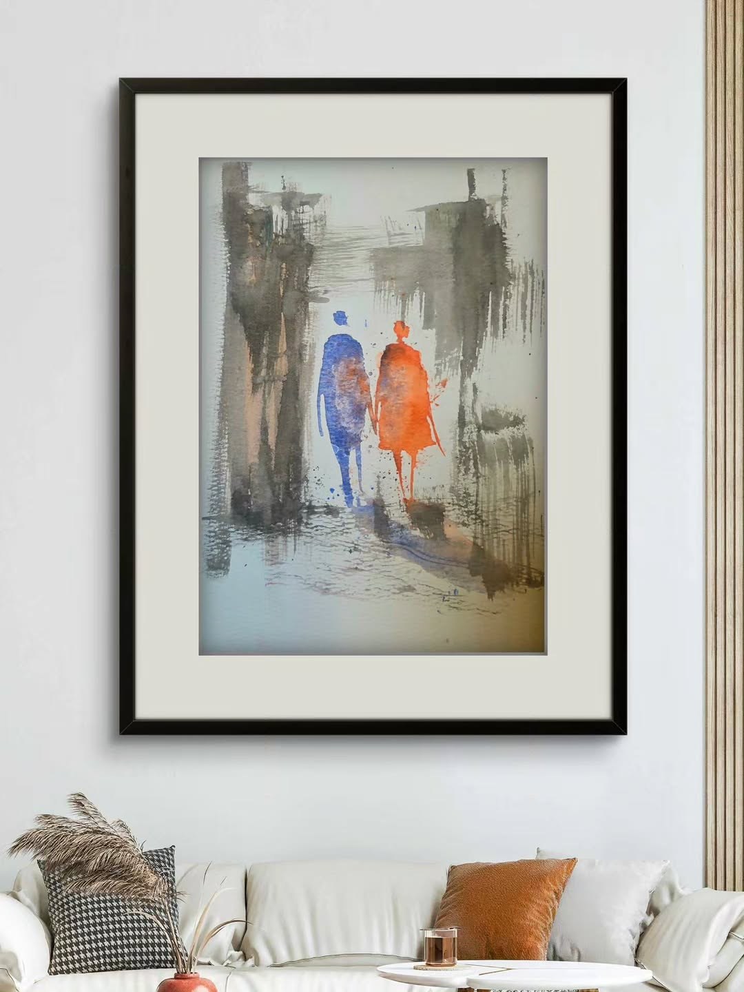 A watercolour painting of two figures walking, framed and hung above a sofa